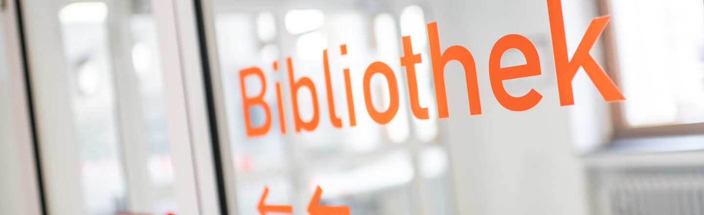 Photo of orange foil lettering "Library" and arrows on a glass door.