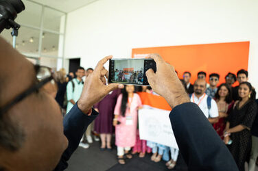 Ein Teilnehmer der International Summer Convention 2024 macht mit seinem Handy ein Foto von einer Gruppe anderer Teilnehmer die eine Flagge ihrer Hochschule hochhalten