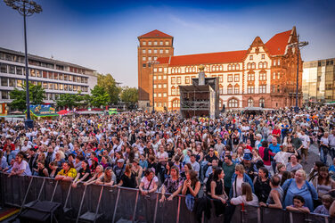 Auf einem Platz vor dem alten Rathaus stehen unzählige Menschen vor einer Absperrung.
