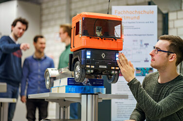 Photo of a model truck in front of which a student is squatting and testing a sensor. Three other people in the background.