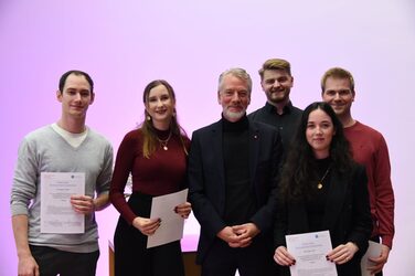 Prof. Helmut Hachul mit fünf Studierenden die ihre Urkunden in der Hand halten auf der Bühne des Hörsaals.