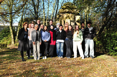 Gruppenbild der Summer School auf der Wiese vor dem Fachbereichsgebäude, im Hintergrund ist das Denkmal zu sehen.