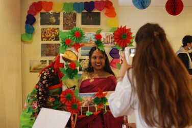 Eine Studentin fotografiert eine andere Studentin, die hinter einem bunt geschmückten Rahmen steht.