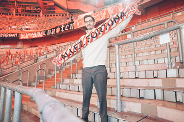 A person stands on the edge of the pitch in a stadium and presents a fan scarf.