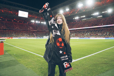 A person stands on the edge of the pitch in a stadium and presents a fan scarf.