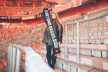 A person stands on the edge of the pitch in a stadium and presents a fan scarf.
