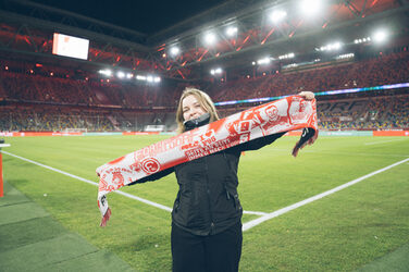 A person stands on the edge of the pitch in a stadium and presents a fan scarf.