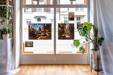 Several pictures are mounted in the exhibition window. To the left and right are tall plants in flower pots.