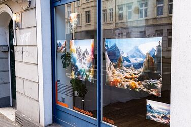 View through the window from outside: There are several pictures in the window depicting mountain landscapes with colorful clouds.