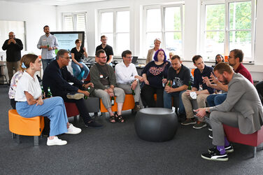 Frontal shot of Mayor Thomas Westphal sitting in a semicircle with other participants in the IDiAL's User Innovation Center and talking.