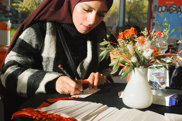 A young Muslim woman writes in the sunlight at a table of a booth__A young Muslim woman writes in the sunlight at a table of a booth