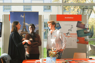 Three women in conversation at an international trade fair stand at the "Marketplace of Opportunities"__Three women in conversation at an international trade fair stand at the "Marketplace of Opportunities"