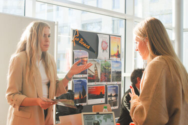 Two young women chat in the sunshine at an international trade fair stand at the "Marketplace of Opportunities"__Two young women chat in the sunshine at an international trade fair stand at the "Marketplace of Opportunities"