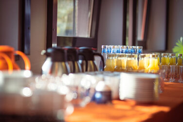 Coffee pots, glasses, plates, cups and orange juice on an orange tablecloth in the sunlight at a buffet__Coffee pots, glasses, plates, cups and orange juice on an orange tablecloth in the sunlight at a buffet