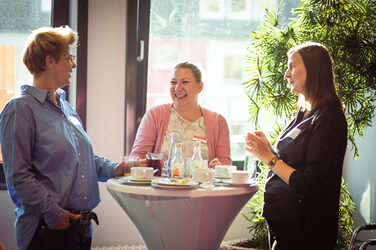 Three people are talking at a bar table in the sunshine, at the welcome event of the international week__Three people are talking at a table in the sunshine, at the welcome event of the international week