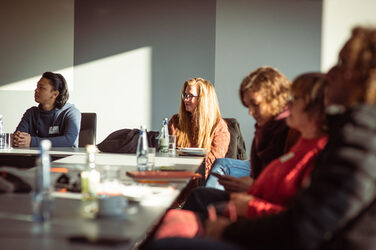 Five people at a conference table look to the left with interest__Five people at a conference table look to the left with interest. The sun shines into the room