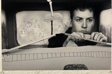 Eine Person sitzt hinter dem Lenkrad eines Auto-Cockpits aus Pappe