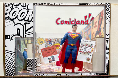 A Superman figure stands in the window of a miniature model of a comic store.