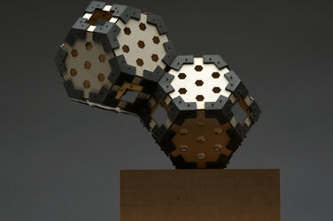 Model of a sculptural hexagon luminaire on a wooden base with generatively manufactured elements against a gray background