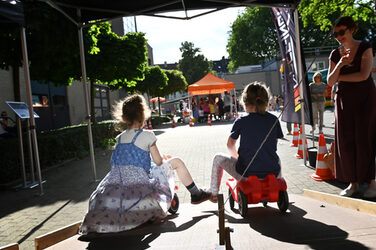 Two children, seen from behind, hurtling down a ramp on bobby cars.