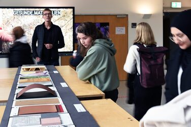 In the foreground, some students can be seen meticulously studying material patterns, while Daniel Horn opens the exhibition at a vernissage