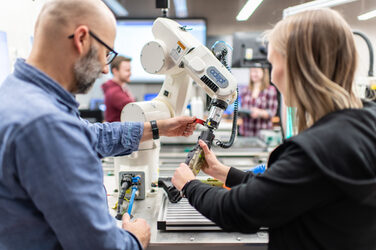 Foto eines Dozenten und einer Studentin, die den Greifarm eines Roboters im Robotiklabor inspizieren.