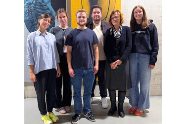 Teilnehmende Studierende und Lehrende des Fachbereichs stehen vor einer Betonwand an der ein Kunstwerk installiert ist.