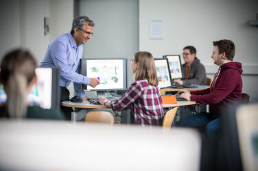 Foto einer Vorlesung des Fachbereichs Machinenbau. Ein Dozierender erklärt Studierenden eine technische Zeichnung an einem Bildschirm.__Photo of a lecture of the Department of Mechanical Engineering. A lecturer explains a technical drawing to students on a screen.