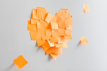 Photo of a heart stuck together from orange sticky notes on the wall. __ A heart stuck together from orange sticky notes on the wall.