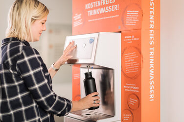 Foto von einer Studentin, die ihre Trinkflasche am FH-Wasserspender mit frischem Wasser befüllt.__Photo of a student filling her water bottle with fresh water at the water dispenser of the Fachhochschule Dortmund.