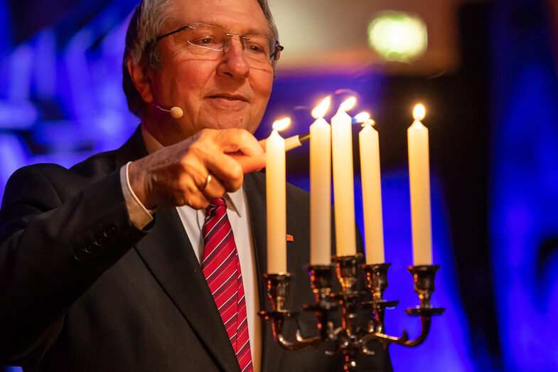 Foto einer männlichen Person. Diese Person zündet fünf Kerzen an, die in einem Kerzenständer stehen.