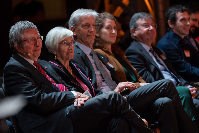 Foto von fünf männlichen und zwei weiblichen Personen, die sitzend in eine Richtung blicken.