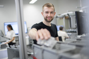 Photo of a student reaching for an item from a container at the workstation in the Lean Lab.