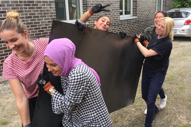 Studentinnen tragen eine Metallplatte vor dem Gebäude der Fachhochschule.