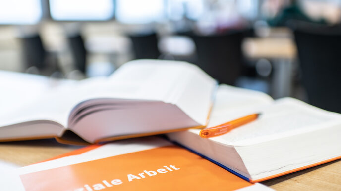 Photo of books lying open on top of each other on the table. In front of them is a booklet with the inscription "Social work".