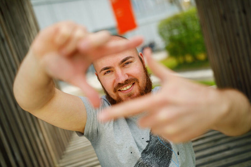 Foto eines Studenten, der mit Zeigefingern und Daumen vor sich ein Quadrat formt und dadurch guckt.