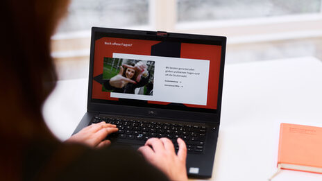 Photo over the shoulder of a person working on a laptop. The slide of a presentation with the title "Any unanswered questions?" is displayed on the laptop.