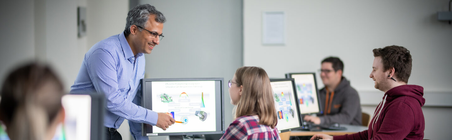 Foto einer Vorlesung des Fachbereichs Machinenbau. Ein Dozierender erklärt Studierenden eine technische Zeichnung an einem Bildschirm.__Photo of a lecture of the Department of Mechanical Engineering. A lecturer explains a technical drawing to students on a screen.