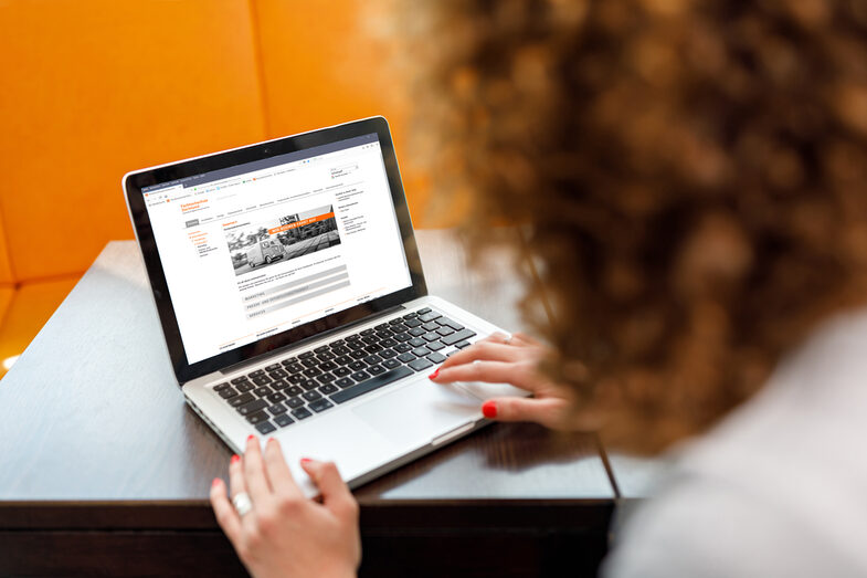 Photo of a young woman at the laptop, in the background there are orange colored chairs. __ Young woman at the laptop, in the background there are orange colored chairs.