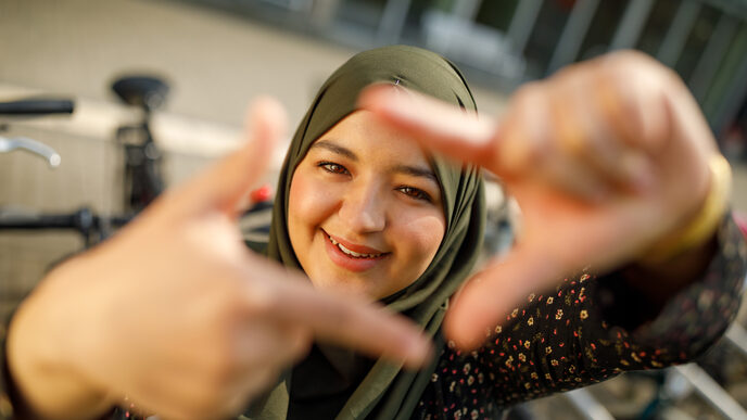 Foto einer Studentin, die mit Zeigefingern und Daumen vor sich ein Quadrat formt und dadurch guckt.