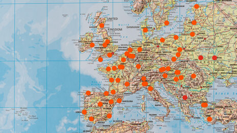 Close-up of a large world map on which places are marked with orange dots.