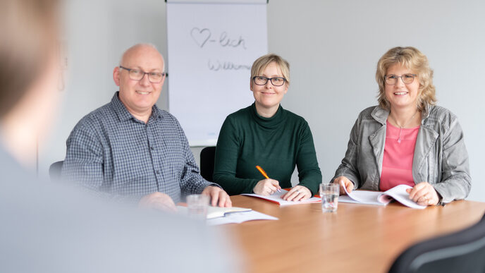 Foto einer Bewerbungsgesprächssituation mit 3 Mitarbeiter*innen der Personalabteilung, die am Tisch nebeneinander sitzen. Ihnen gegenüber sitzt eine Bewerberin - im Bild stark unscharf und im Anschnitt. __ <br>Job interview situation with 3 employees of the HR department who are sitting next to each other at the table. An applicant is sitting across from you - in the picture very blurred and in a bleed.