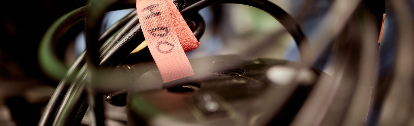 Foto von Kabeln, die mit einem orangefarbenen Klettband zusammengebundene sind, auf dem "FH DO" steht. __ Cable with an orange Velcro tape that says "FH DO".