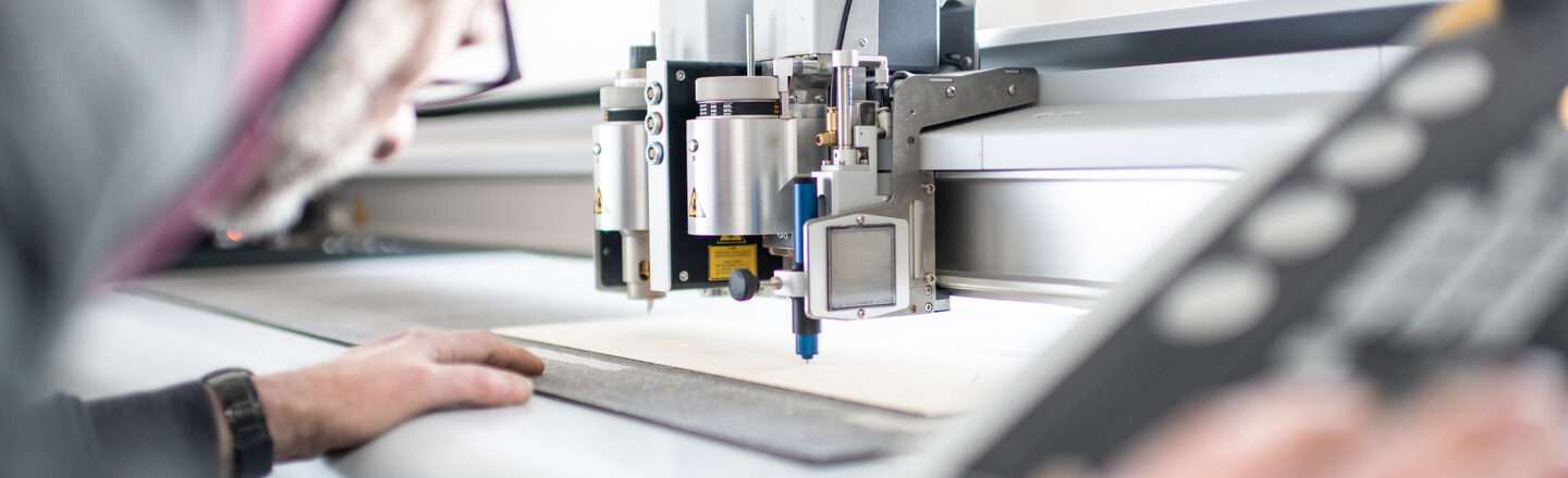 Photo of a man working on the laser cutter and cutting a panel to size.