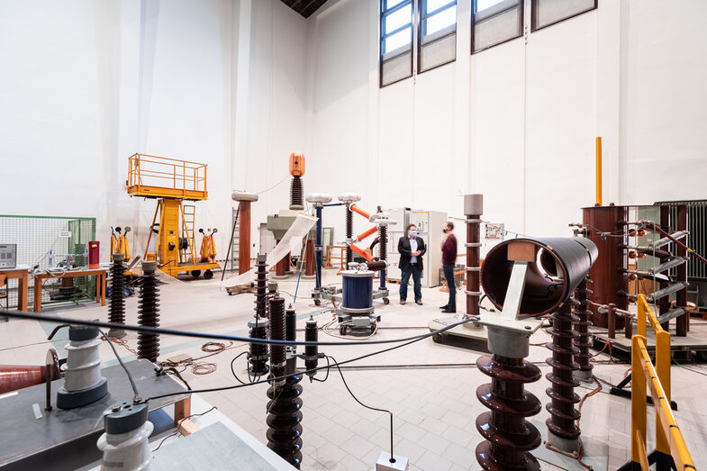 Room shot of the high-voltage laboratory with a wide range of laboratory equipment. Two men are standing in the middle of the laboratory talking. __