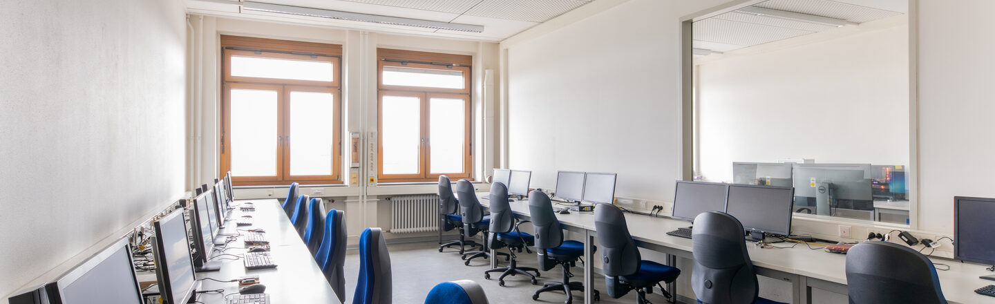 Room shot of a laboratory with tables and computer workstations, lined up on the right and left of the wall.