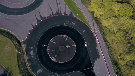 Bird's eye view of a circular track with irrigation. Test vehicles (Volvo, Spyder) are driving on it.