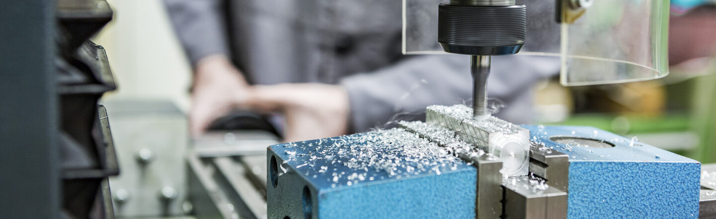 Photo of a person working with a milling machine in the mechanical workshop. The machine is milling something into a piece of metal.