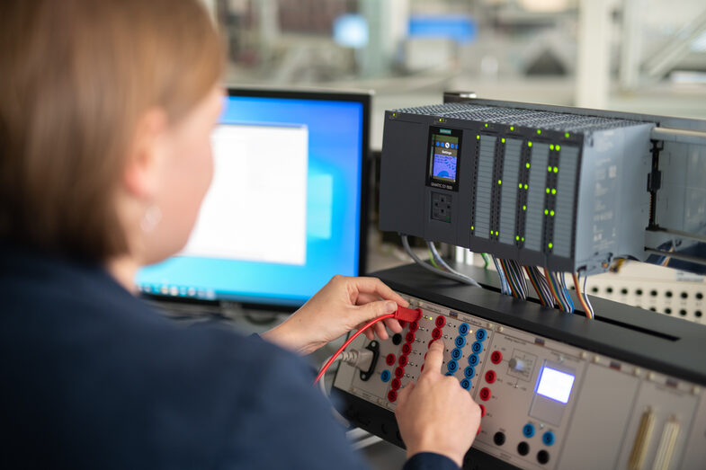 Cropped photo of a woman plugging a cable into a control device. Next to it is a PC screen.