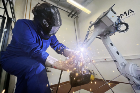 Person with self-developed, 3D-printed gripper, can be seen behind a shower of sparks underneath the gloves, holding the rod in position with the robotic arm.